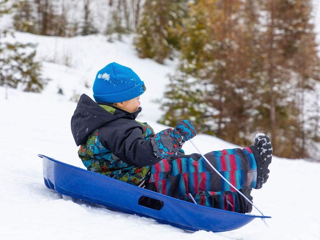 Child model riding blue plastic sled in snow