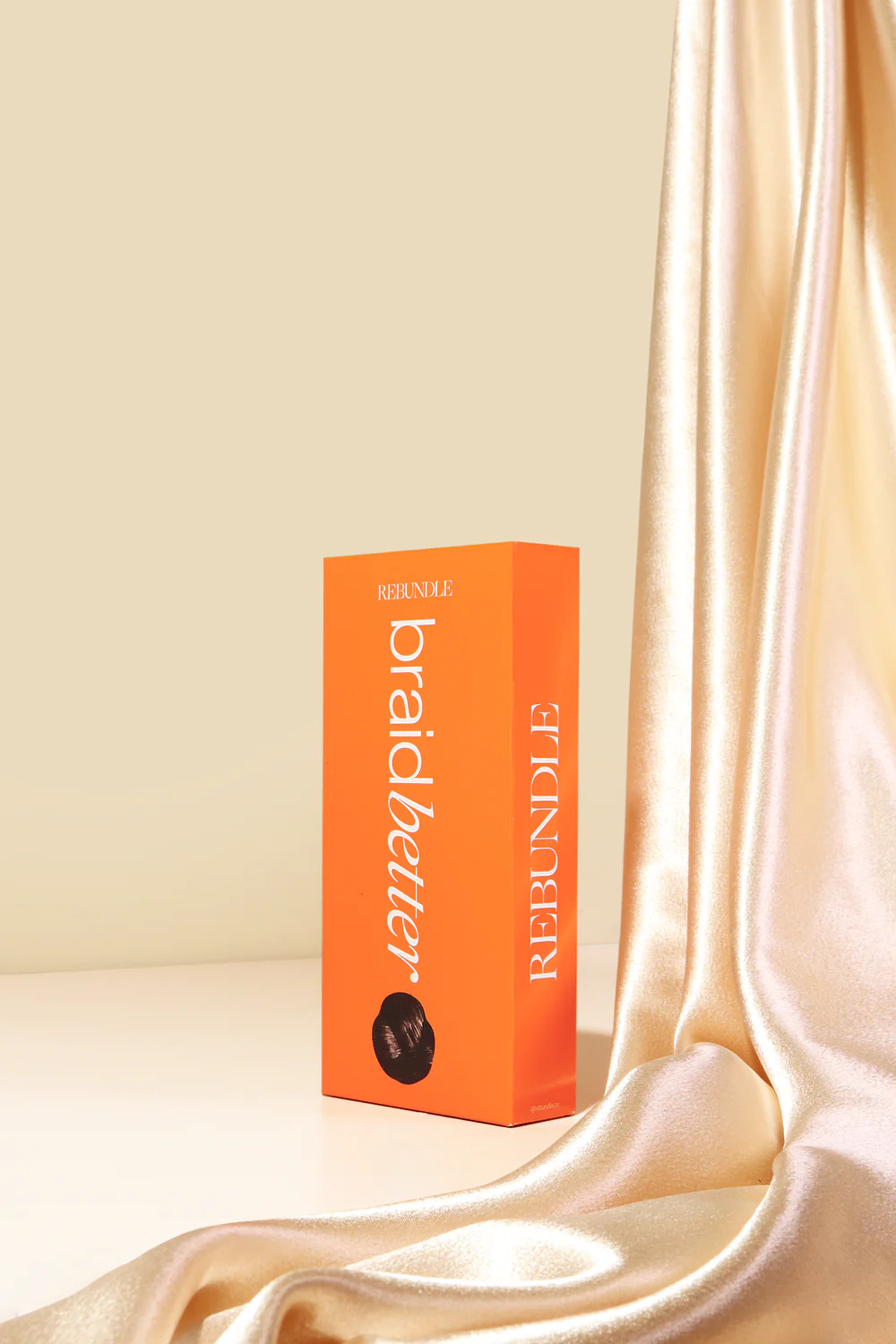 Rebundle Braidbetter hairsbreadth  merchandise  container  displayed adjacent  to silky cloth  drape, suggesting luxury and style