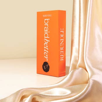 Rebundle Braidbetter hairsbreadth merchandise container displayed adjacent to silky cloth drape, suggesting luxury and style