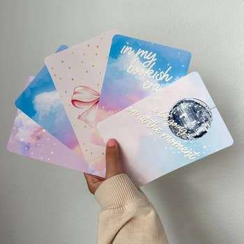 Person holding a set of illustrated cards with various pastel and disco designs 