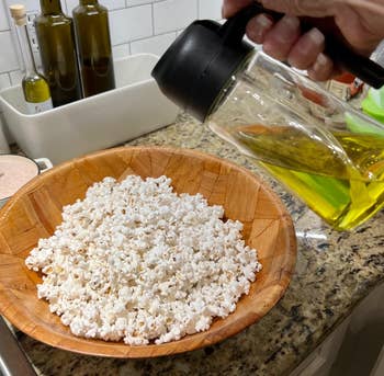 reviewer pouring olive lipid onto a vessel of popcorn with the sprayer bottle