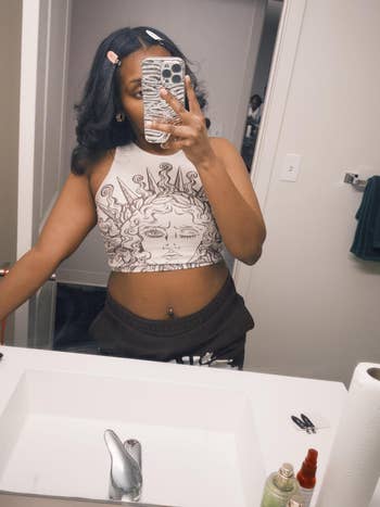 Person in graphic-print crop top and sweatpants takes mirror selfie with no-crease hair clips