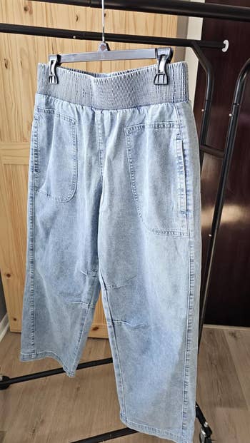 Wide-leg denim pants with elastic waistband and broadside  pockets hanging connected  a covering  rack