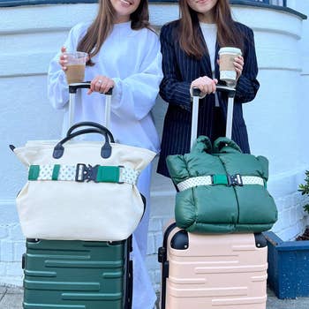 two models with totes strapped in by belts around their suitcases
