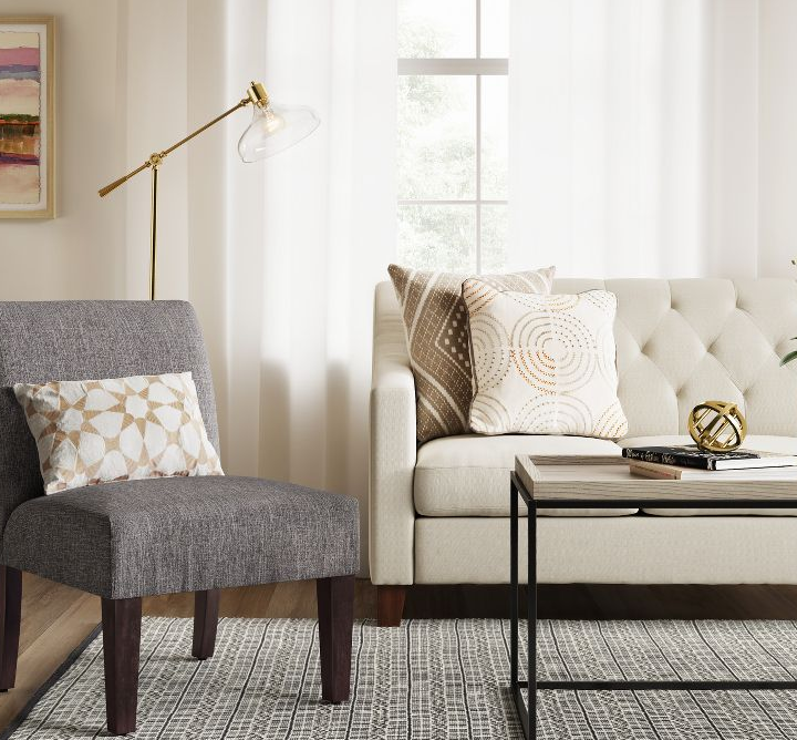 灰色拖鞋椅子，带有图案的掷枕头，旁边是客厅的奶油色沙发“class=