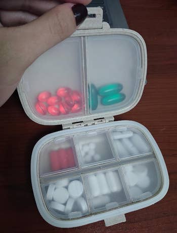 Hand holding open a pill organizer with various medications in compartments, highlighting organization for health management
