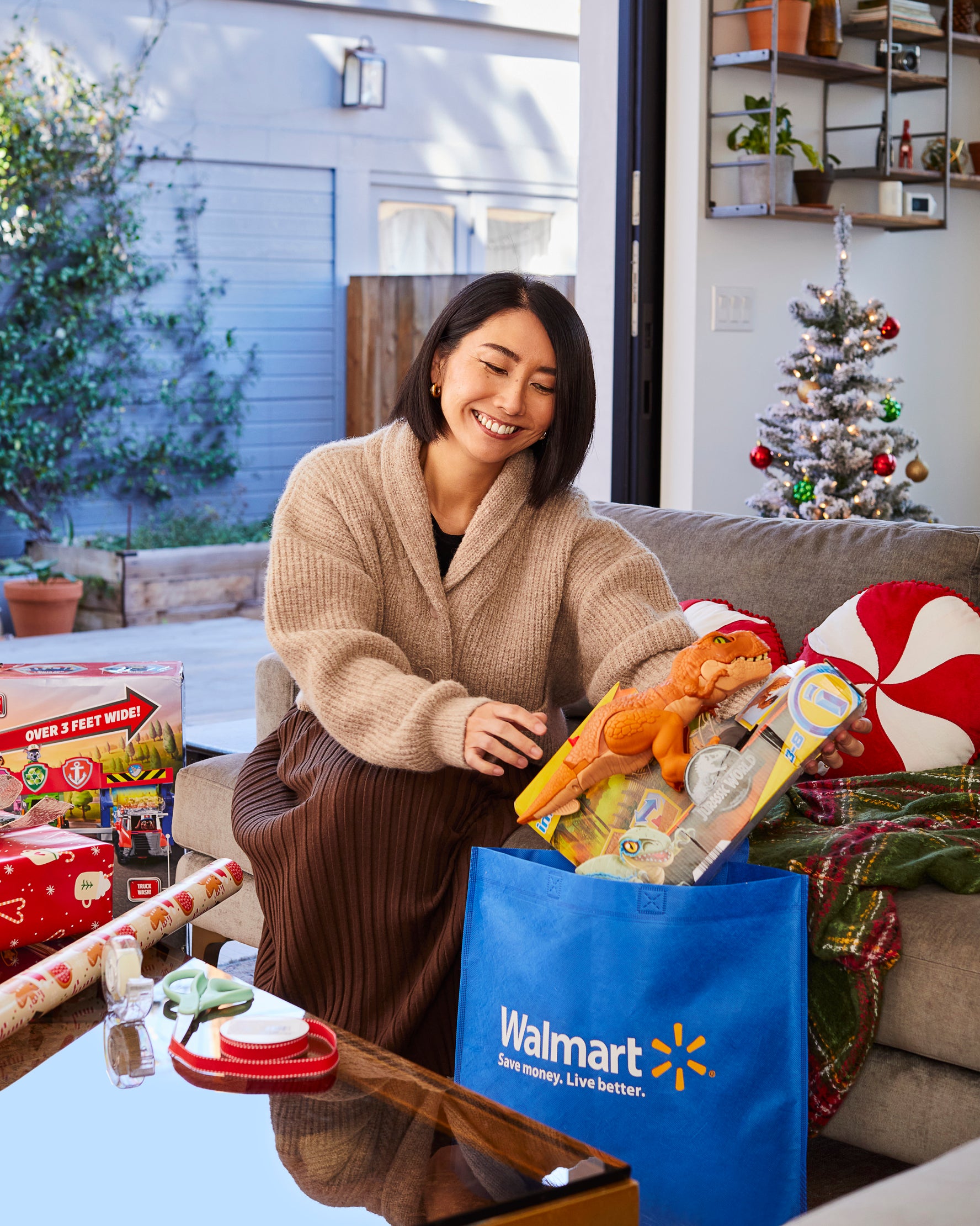 Rie pulls dinosaur toy out of Walmart bag in living room decorated with Christmas tree