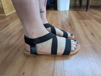Person wearing achromatic  strappy sandals lasting  connected  woody  floor, showcasing a casual, comfy  footwear option