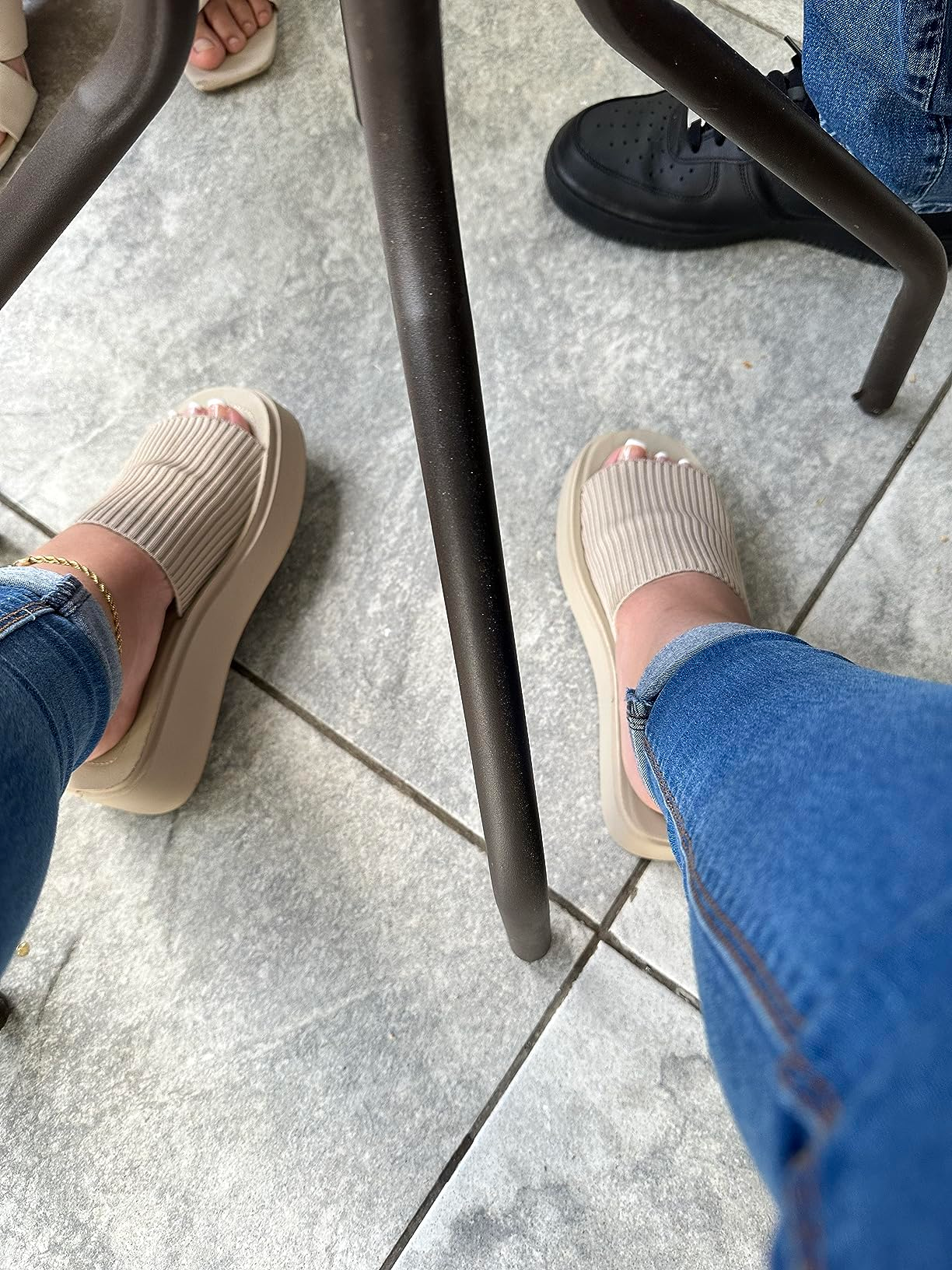A idiosyncratic   wearing ribbed descent  sandals and jeans is seated astatine  an outdoor array  adjacent   idiosyncratic    successful  achromatic  shoes
