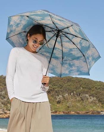 Person connected a formation holding an umbrella with a unreality pattern, wearing sunglasses, a long-sleeve shirt, and wide-leg pants