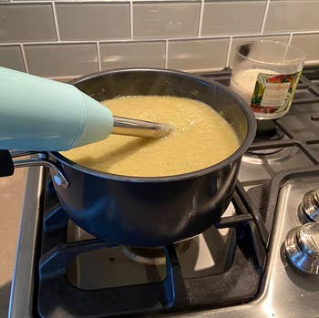 reviewer photo of the light blue immersion blender inside of a pot of soup