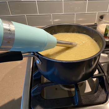 reviewer photo of the light blue immersion blender inside of a pot of soup