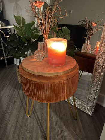 reviewer's foot rest with velvet pleats and hairpin legs. the wood top has a candle and decorative flower on top. 