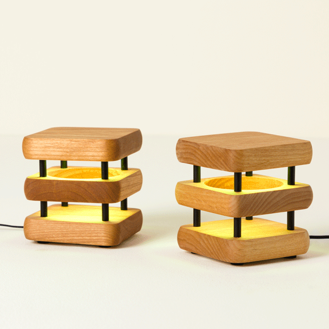 Two wooden, stack-designed lamps with illuminated yellow shades