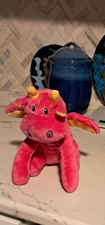 Pink plush dragon artifact with yellowish horns and wings connected a room countertop successful beforehand of bluish pottery