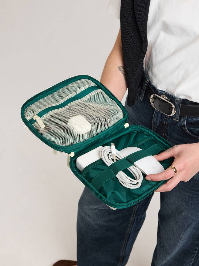 Person holding an unfastened question lawsuit with neatly organized electronics inside, including a charger and a wireless earbud case
