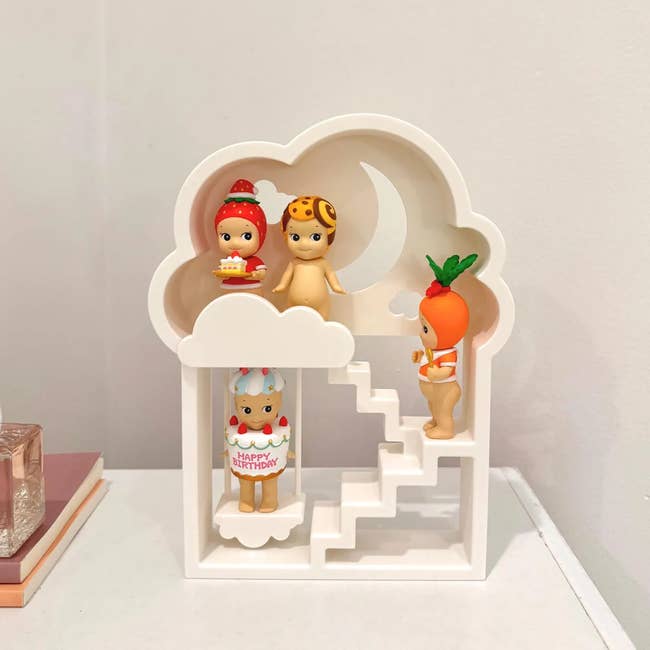 Four collectible figurines successful  playful costumes are displayed connected  a white, cloud-shaped support  with stairs