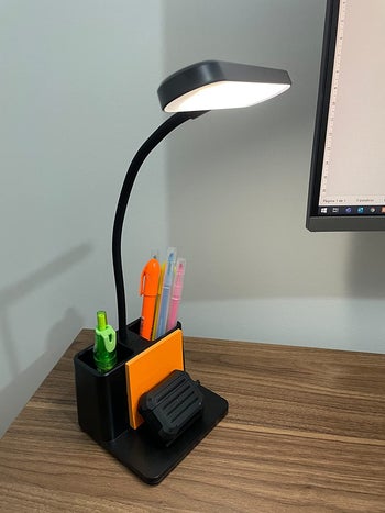 Reviewer's black LED desk lamp on their desk filled with pens and the stand holding their pager and some sticky notes