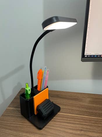 Reviewer's black LED desk lamp on their desk filled with pens and the stand holding their pager and some sticky notes