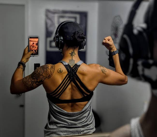 Reviewer showing the back of a gray tank top with an open back showing black criss crossing bra straps 