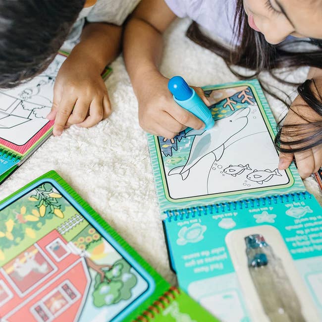 two kids using reusable water pens to color on the reusable pages