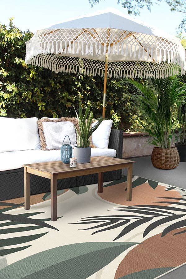 a patio setup with the abstract palm leaf inspired rug, a couch, table decor and outdoor umbrella