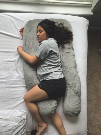 A reviewer laying between the pillow with one leg and arm under and one over