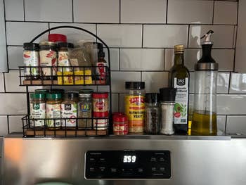 Kitchen counter with spice rack featuring various spices and cooking oils, including olive oil and nutritional yeast, against tiled backsplash