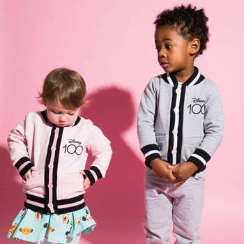 two child models wearing disney 100 bomber jackets