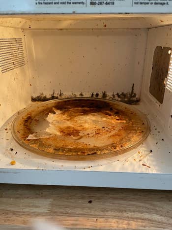 A dirty microwave interior with food splatters and a stained turntable
