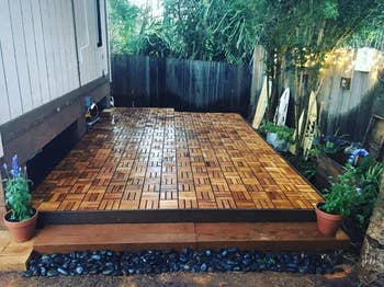 Wooden patio platform  with interlocking tiles, surrounded by potted plants. Suitable for stylish outdoor gatherings