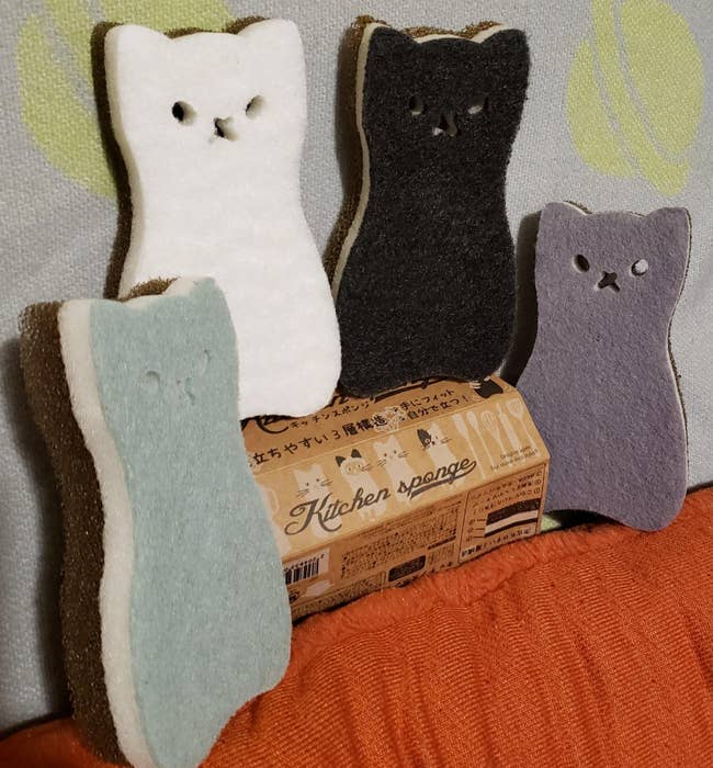 four cat-shaped sponges in blue, lavender, white, and black 