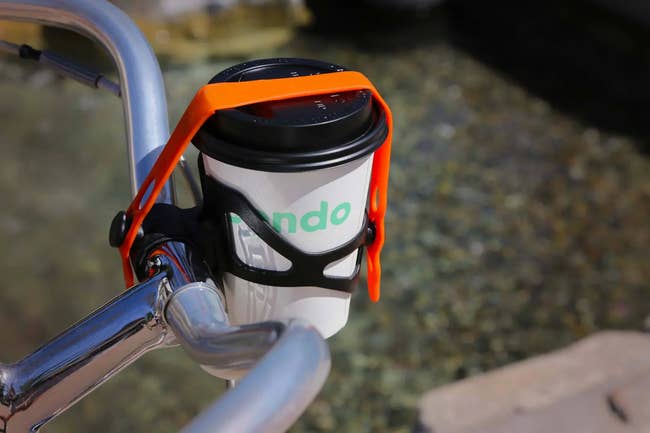 A cup of coffee in a holder on front handle bars with a silicone strap securing it 