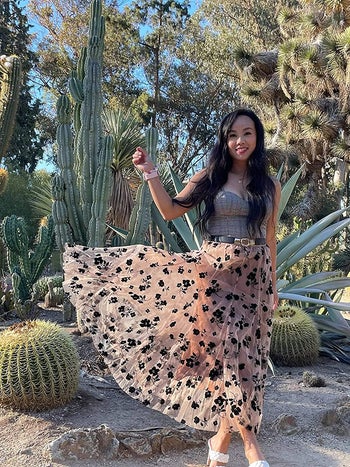 Reviewer is wearing a very light pink flowy skirt with black floral pattern on it