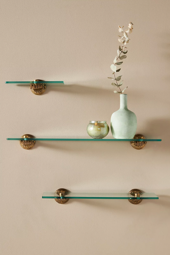 Three glass shelves with bronze hand-shaped holders on a white wall with vases 