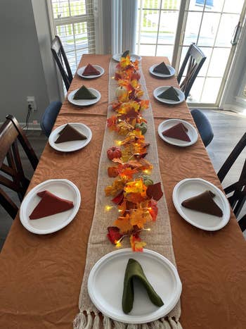 Table acceptable   for autumn  with a cloth runner, autumn leaves, mini pumpkins, and triangular napkins connected  plates, suggesting a cozy, seasonal eating  experience