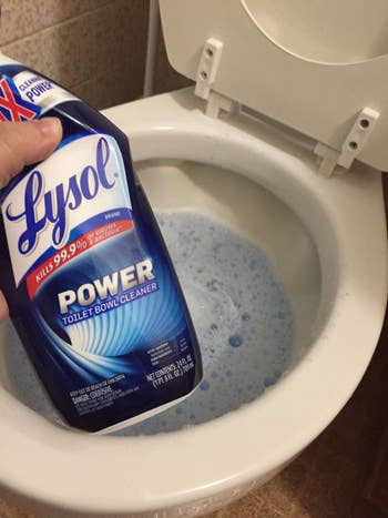 reviewer holding a bottle of Lysol Power Toilet Bowl Cleaner over an open toilet bowl filled with blue gel