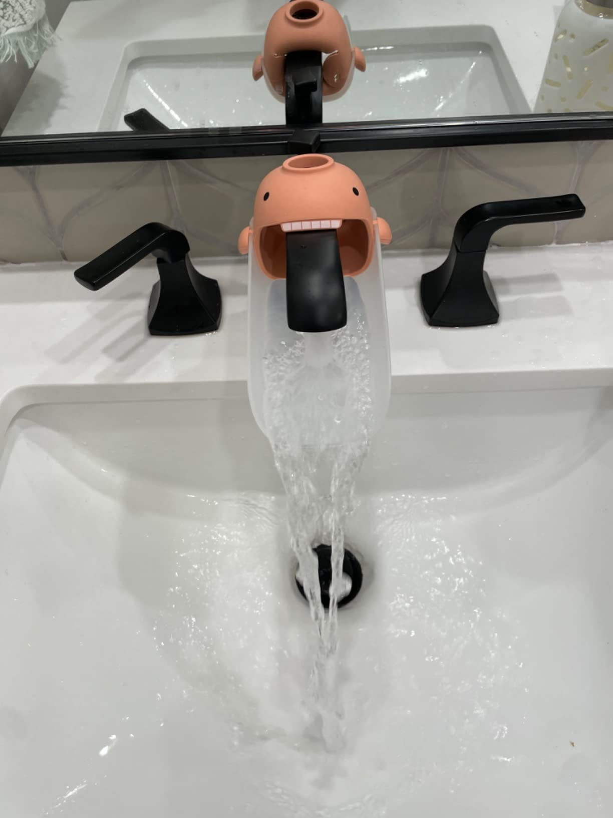 Water flows from a playful, character-shaped faucet extender into a sink, promoting child-friendly bathroom accessories
