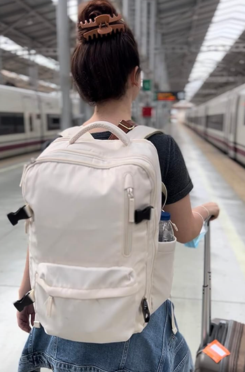 Reviewer carrying white backpack with front pocket and water bottle side sleeve in an airport 