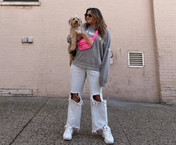 person wearing hot pink fanny pack with jeans and sweatshirt while holding dog