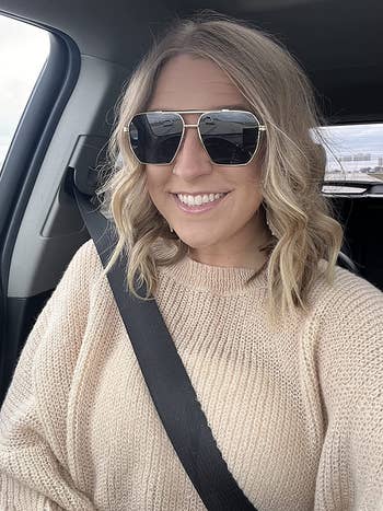 a reviewer wearing the gold frame sunglasses in a car