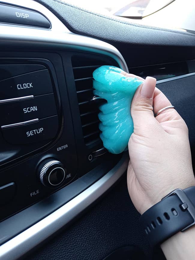 hand smushing blue cleaning gel into a car's air vent