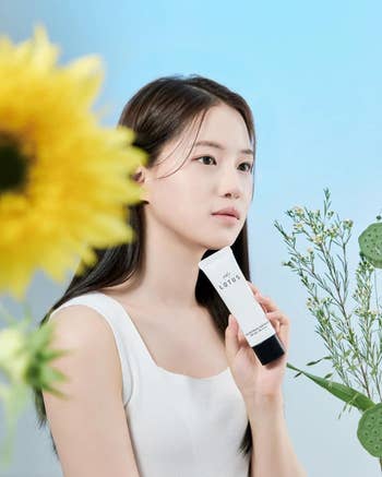 model holding the tube of sun cream while surrounded by plants