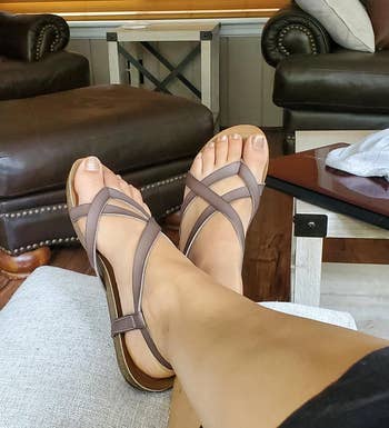 reviewer wearing brown strappy sandals, showcasing them with crossed legs in a living room setting