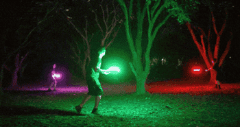 a group of people tossing the light-up frisbees around at night
