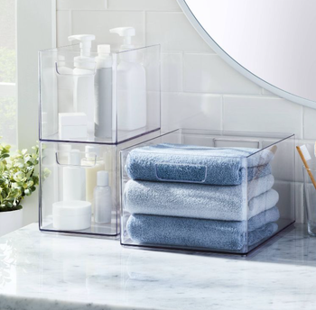 three clear bathroom organizers with lotions / towels inside