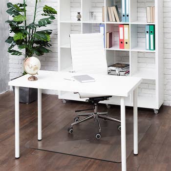 a white desk setup and bookshelf with the clear mat on hard wood