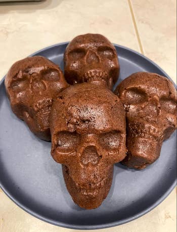 Four skull-shaped chocolate muffins on a dark plate