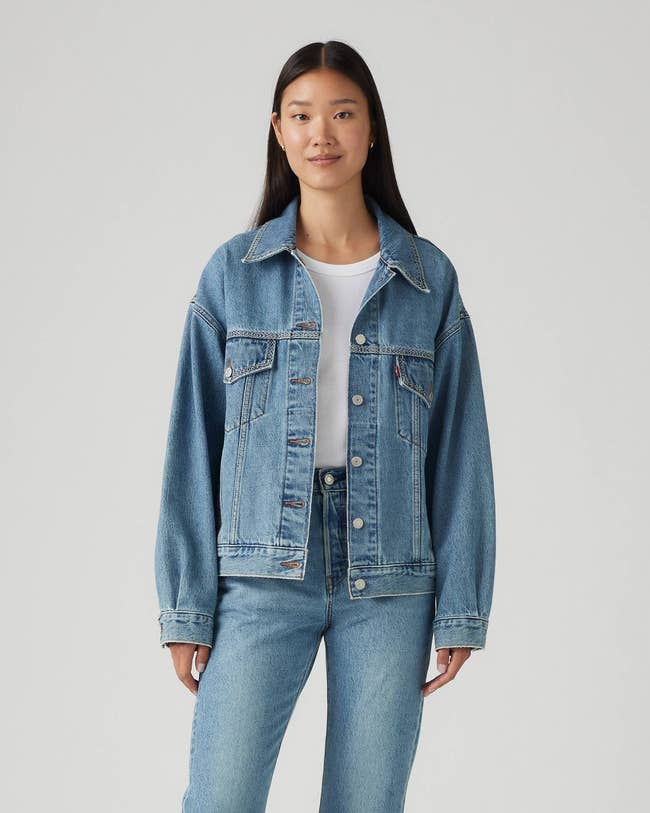 Person wearing a denim jacket over a white shirt with matching jeans, posing against a plain background