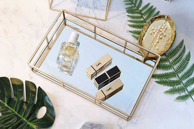 the gold mirror tray holding perfume and lipsticks